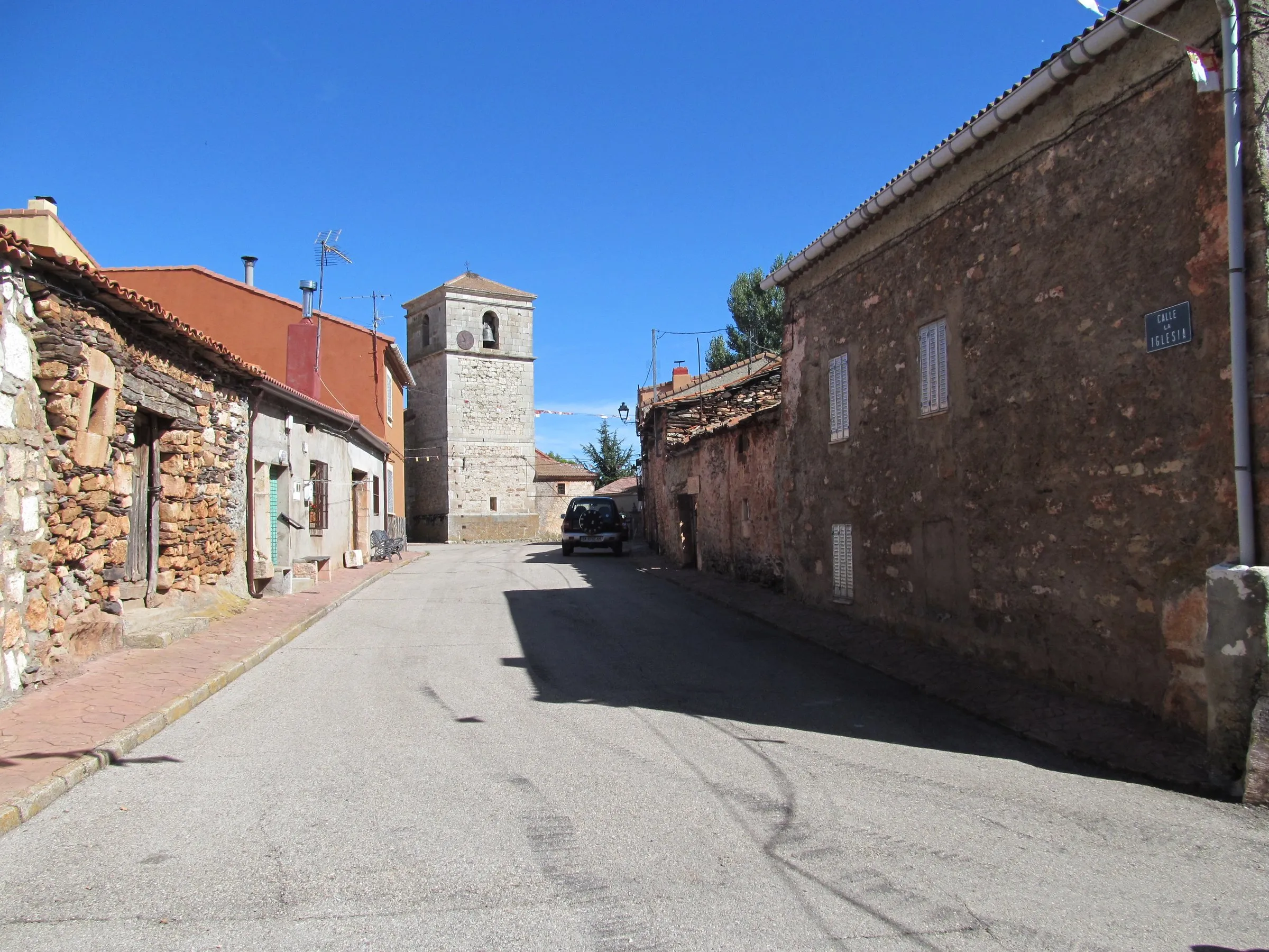 La calle Mayor de Cantalojas, con casas de piedra a los lados y la torre de la iglesia de San Julián al fondo