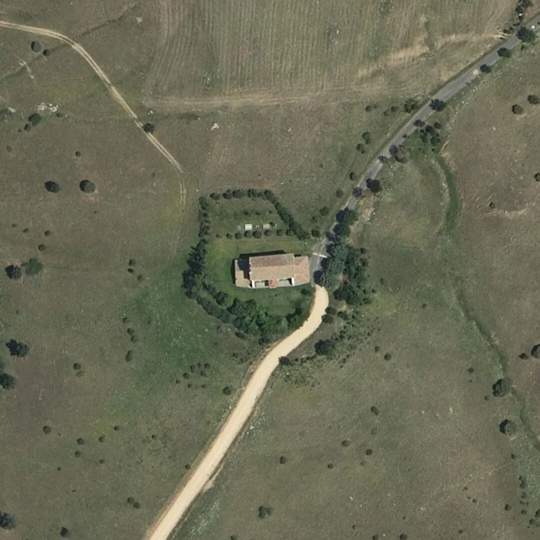 La ermita de Cerezuelo vista desde el aire: la nave de teja en un prado cercado por un seto, junto al camino, entre pastos con encinas sueltas
