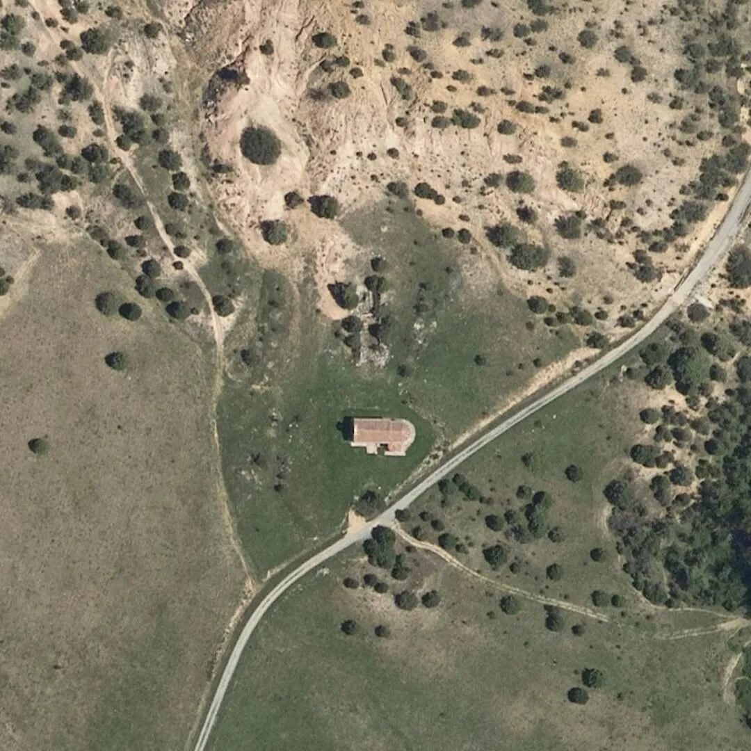 La ermita de la Varga vista desde el aire: la nave de teja con su ábside redondo, en un prado junto al camino, con la ladera de yeso blanquecina detrás