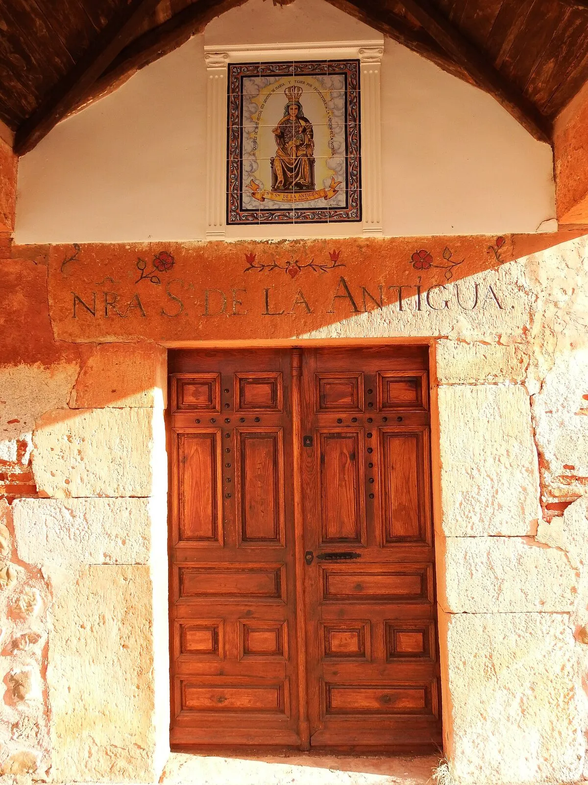 El dintel de la ermita de Ribota, con «Nra Sª de la Antigua» grabado y flores pintadas, y encima un panel de azulejos con la Virgen