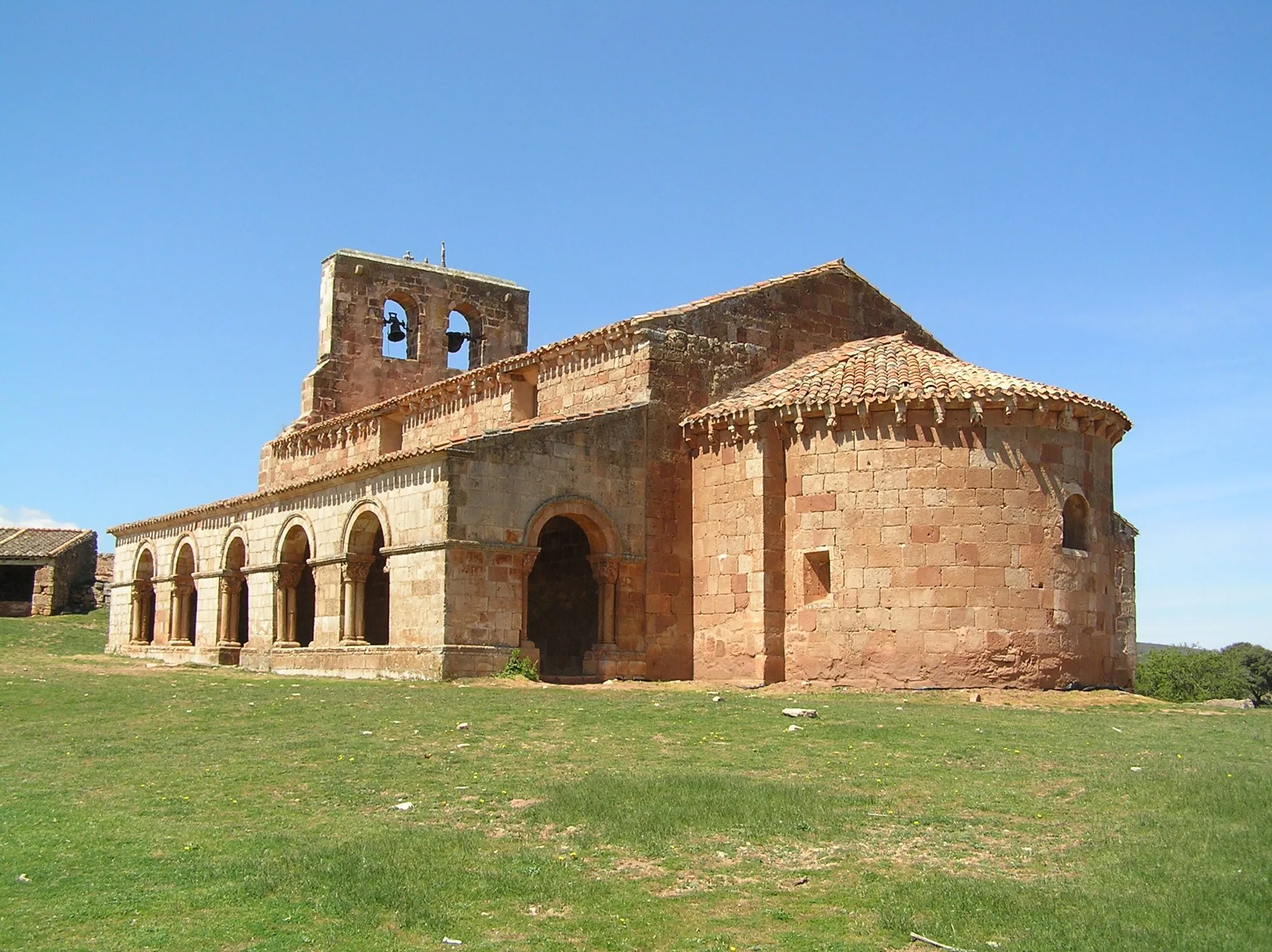 La ermita de Santa María de Tiermes, con su galería porticada de arcos y el ábside de piedra rojiza, sobre la pradera