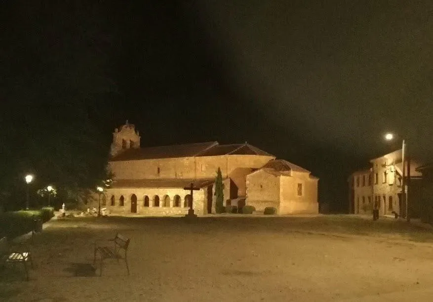 La iglesia de noche, con el pórtico iluminado y la plaza en penumbra