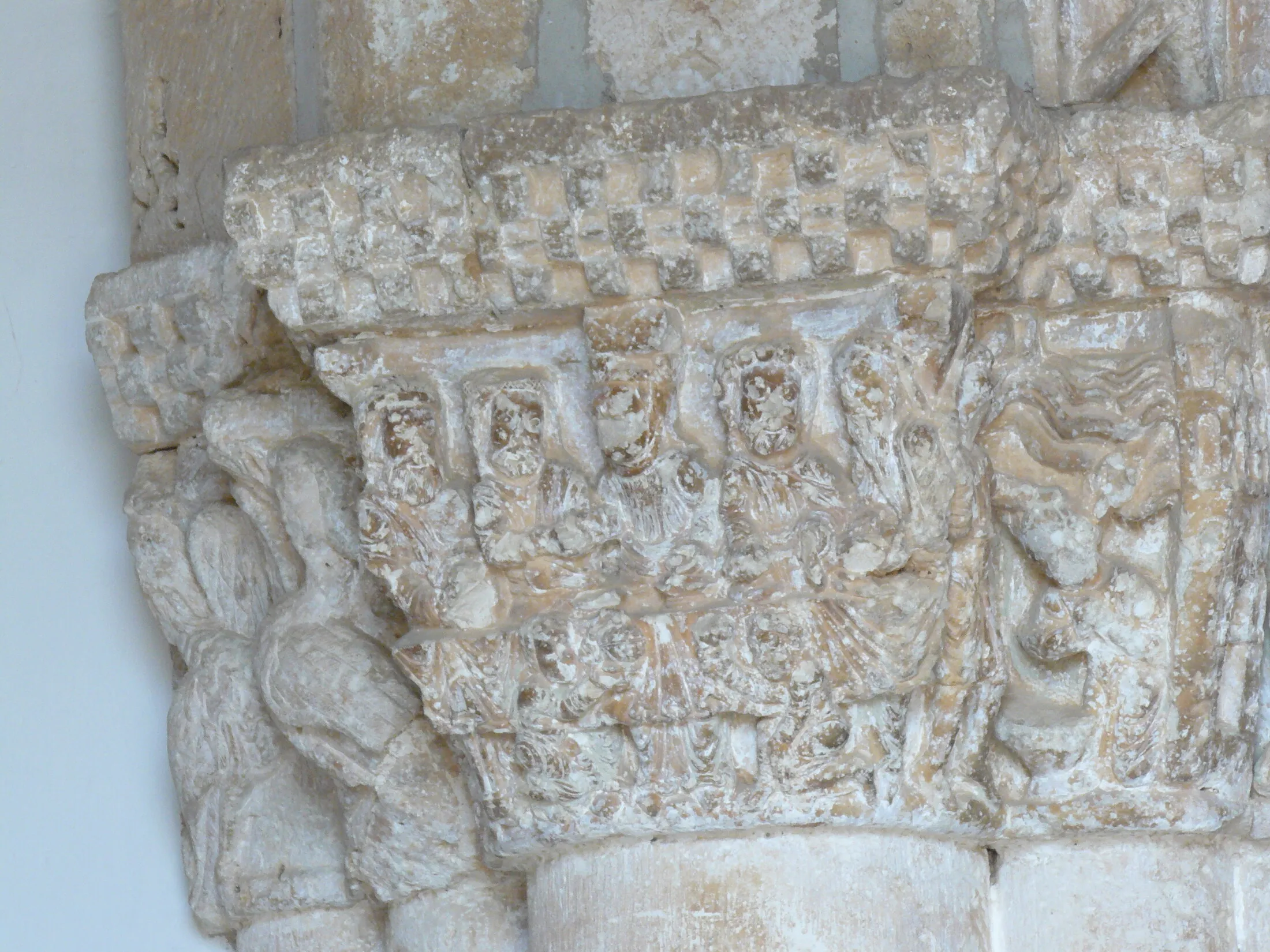 Capiteles románicos de la portada de Languilla: figuras sentadas tras una mesa con mantel labrado, bajo un cimacio de ajedrezado, y a la izquierda dos figuras con cuerpo de ave