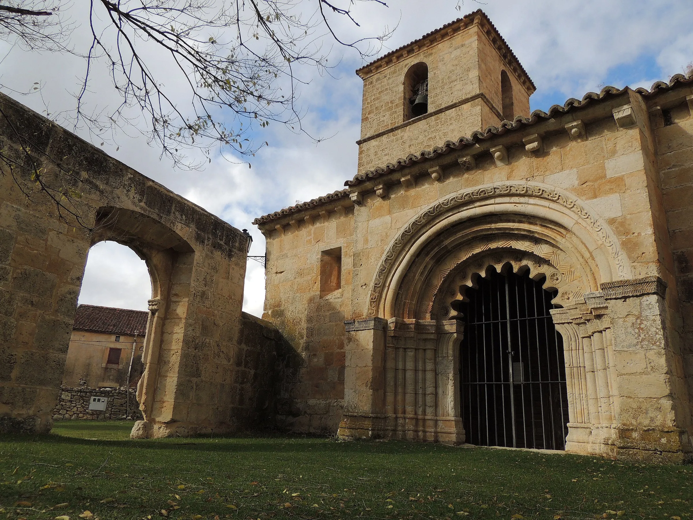 La portada románica y la torre de la iglesia de San Pedro de Villacadima, con un arco de piedra a la izquierda