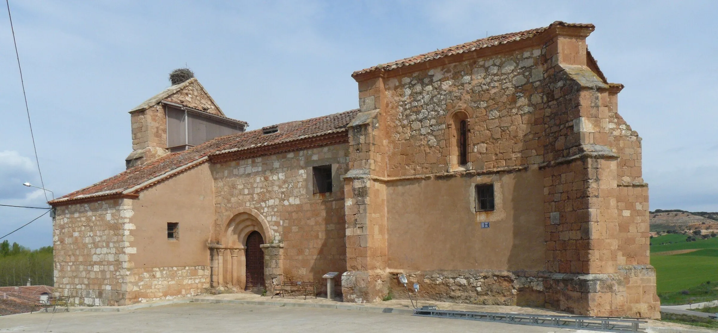 La iglesia de San Juan Bautista de Mazagatos, de sillería y mampostería rojiza, con la portada románica en el muro sur, la cabecera alta con una ventana de medio punto y la espadaña con un nido de cigüeña