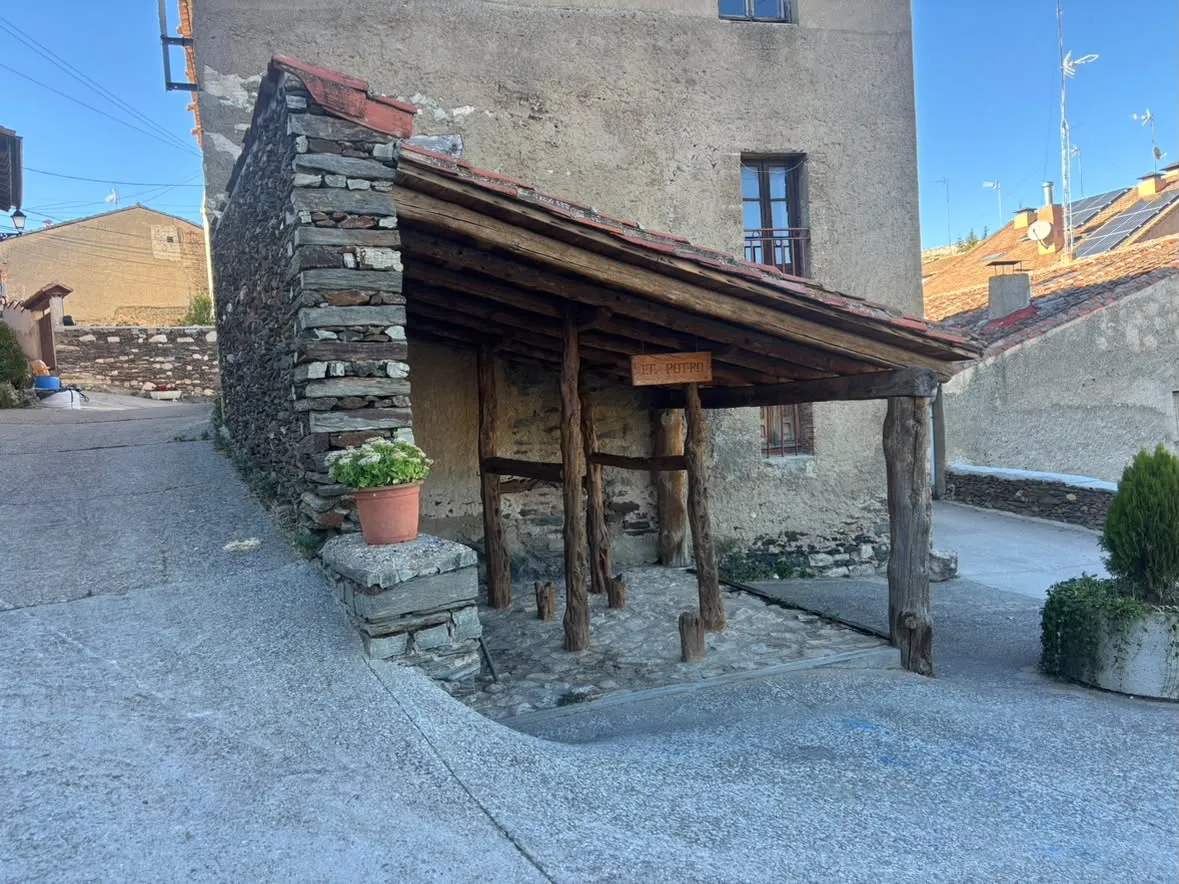 El potro de herrar de Grado del Pico bajo su tejadillo de teja árabe, arrimado a un muro de pizarra, con un letrero de madera que dice «El potro»