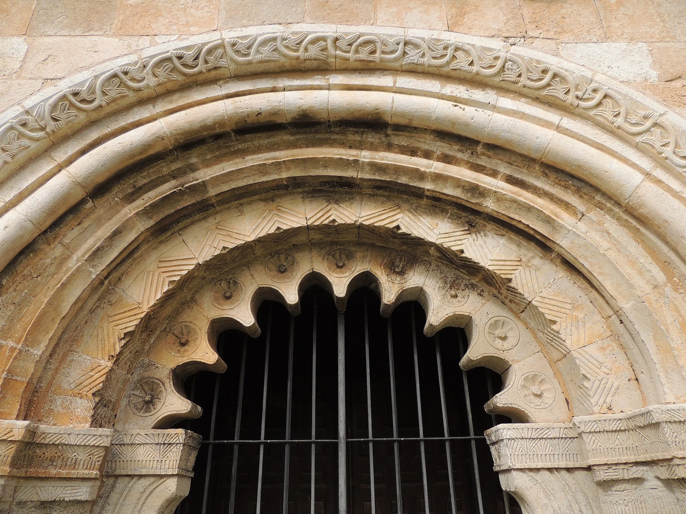 La portada de San Pedro de Villacadima de cerca: el arco lobulado de la entrada, la arquivolta de zigzag y el guardapolvo de tallos